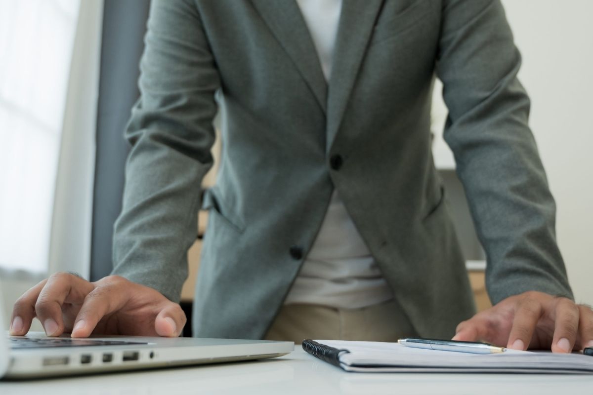 Profesionalac duboko zamišljen kuca na laptopu dok priprema beleške za važan sastanak.